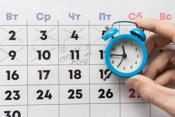 一只手拿着一个小闹钟 后面是一个日历 上面标着一天和假期 — 图库照片