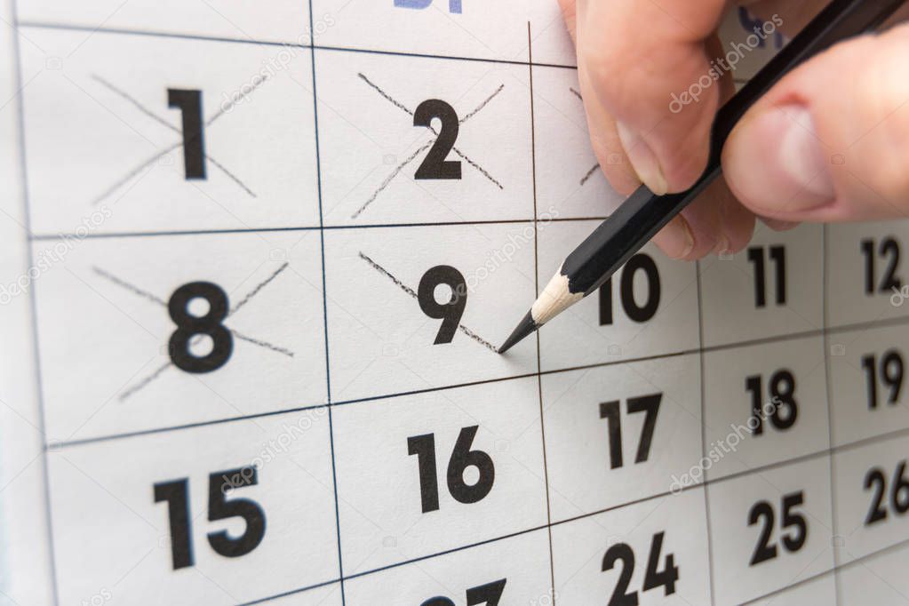 Pencil crosses out dates on the wall calendar