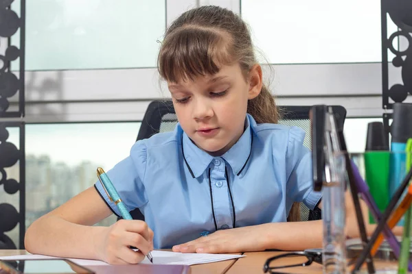 Egy nyolc éves lány koncentrál az írásra egy töltőtollal az asztalnál egy irodában. — Stock Fotó