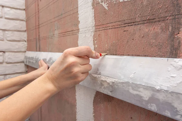 Рука рисует горизонтальную линию карандашом на стене, используя алюминиевое правило — стоковое фото