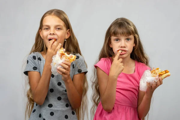 Duas meninas são engraçadas comendo pão, empurrando comida em sua boca com os dedos — Fotografia de Stock