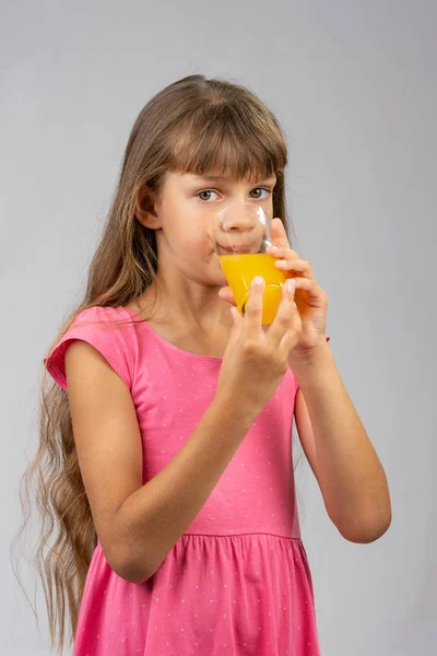 The girl drinks orange juice from a glass and looks at the frame — Stock Photo, Image