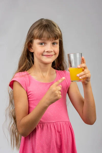 Ein Mädchen hält ein Glas Orangensaft in der Hand und zeigt mit dem Finger darauf — Stockfoto
