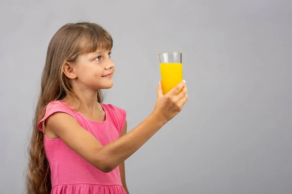 A girl holds a glass of juice in her hand and looks at the empty space on the right — Stock Photo, Image