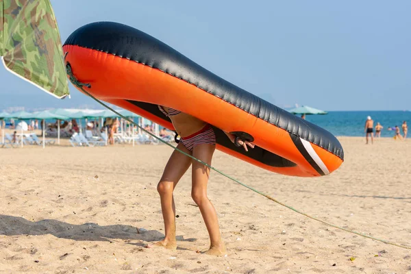 Tini lány magával ránat a hátán egy nagy felfújható csónak a homokos strandon — Stock Fotó
