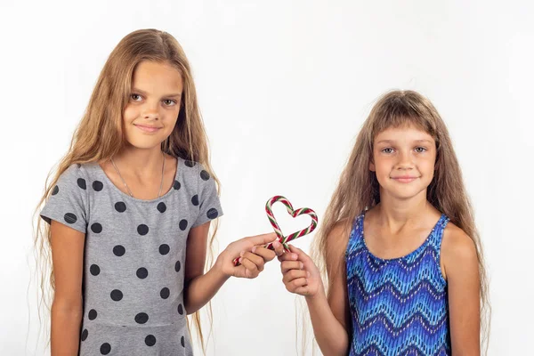 Duas meninas fizeram um coração de dois pirulitos e olham para a moldura — Fotografia de Stock