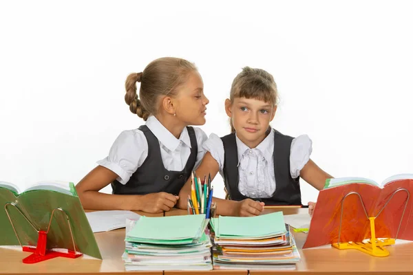 Meninas estão sentadas em uma mesa da escola, um sussurra para o outro algo no ouvido — Fotografia de Stock