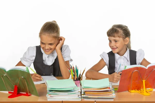 Twee schoolmeisjes zitten aan een bureau en kijken vrolijk naar het schoolboek — Stockfoto