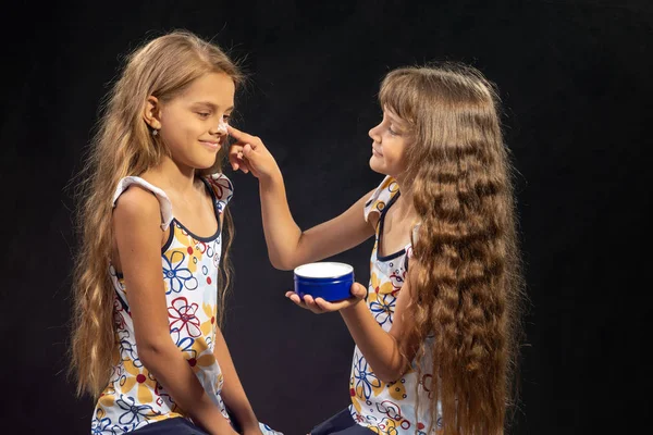 Menina coloca creme no nariz de sua irmã — Fotografia de Stock