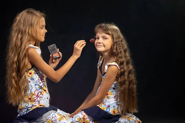 The older sister is applying powder to the younger girl's face — Stock Photo, Image