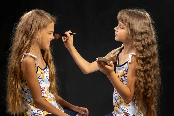 Girl powdering with a brush a nose to another girl, studio, black background — Stock Photo, Image
