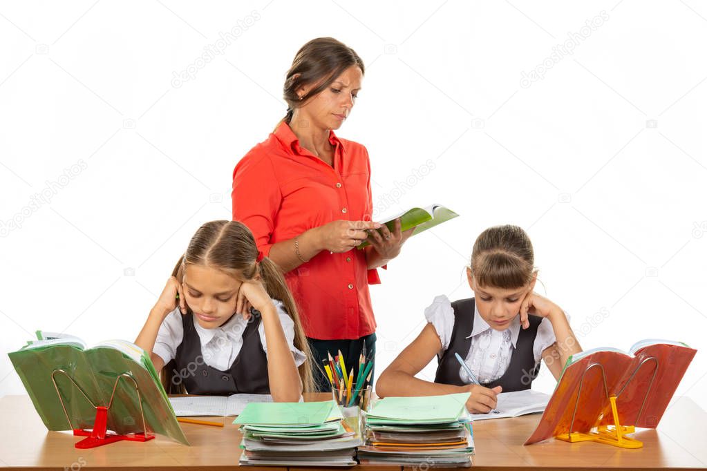 Schoolchildren at the desk do the assignment, the teacher in the background reads the assignment