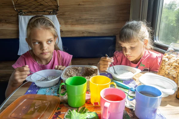 Due ragazze mangiano il grano saraceno con latte da stoviglie usa e getta di plastica su un treno — Foto Stock