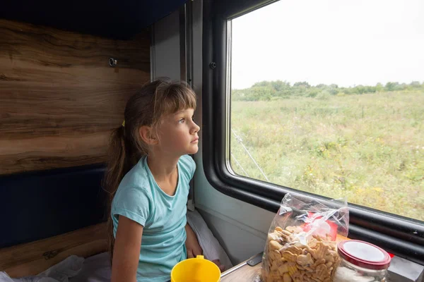 Ayrılmış bir koltuk vagonunda oturan kız pencereden yorgun dışarı bakıyor — Stok fotoğraf