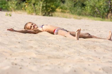 Teen girl sunbathes alone on a river sandy river beach clipart