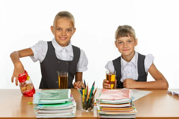 Dos amigas de la escuela beben jugo y comen galletas en una mesa en una clase escolar — Foto de Stock