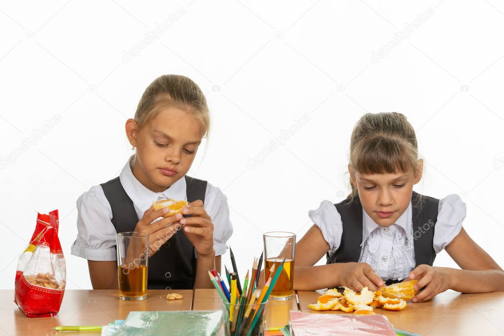 Two tired schoolgirls at recess eat an orange and drink juice
