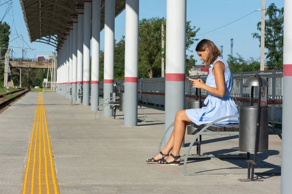 Девушка смотрит на телефон на пустой платформе железнодорожного вокзала — стоковое фото