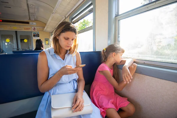 Молодая девушка смотрит на телефон, дочь на окно в электричке — стоковое фото
