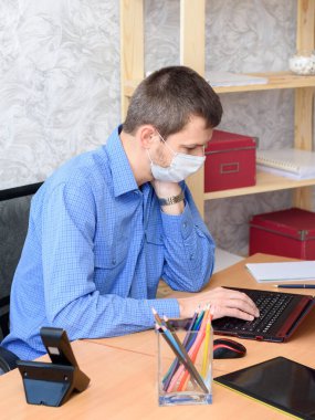 Bir ofis çalışanı tıbbi maske takarak masada oturuyor.