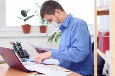 Maskeli bir ofis çalışanı masaüstündeki belgeleri söker