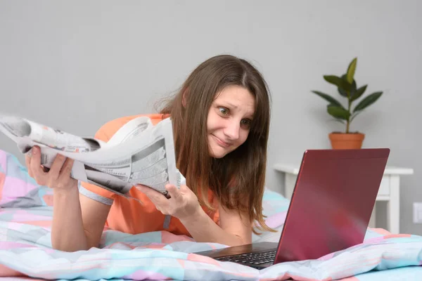 Girl Newspapers Her Hands Lies Bed Looks Laptop Screen Search — Stock Photo, Image