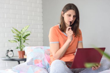 Kız video dersi izliyor ve düşünceli bir şekilde kalemi kemiriyor.