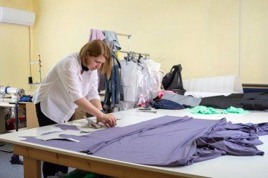 Moda tasarımcısı atölyedeki giysi detaylarını kesiyor.