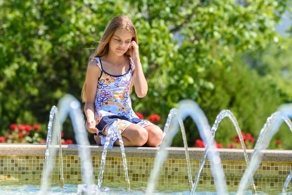 一个女孩坐在喷泉边 看着水柱 — 图库照片