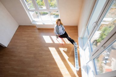 Yukarıdan bir kızın sandalyeye oturduğu geniş pencereli büyük bir odaya bak.