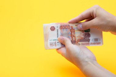 Sarı arka planda beş bininci Rus rublesini tutan iki el.
