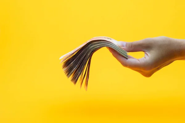 Hand holds out a wad of money, yellow background