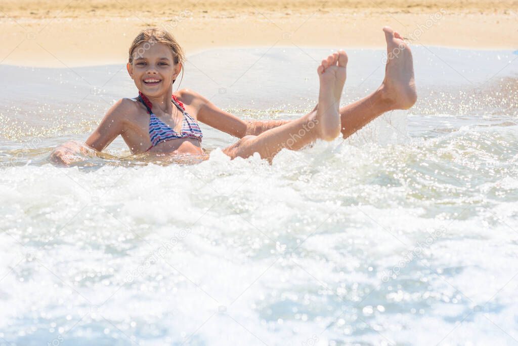 Girl swims in the waves on the sandy seashore