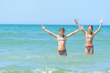 Çocuklar deniz suyunda durur ve sevinçle ellerini kaldırır.