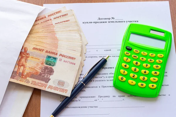 Masanın üzerinde arsa satışı için bir sözleşme var. Zarfın içinde bir tomar para, bir kalem ve bir hesap makinesi.