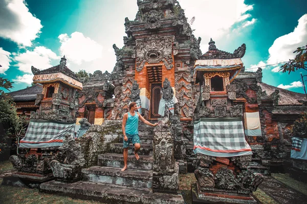 A man in a blue T-shirt near an ancient stone building bali indonesia