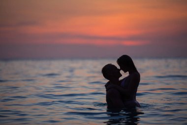 Gün batımında öpüşmeden önce denizde yüzen romantik bir çiftin silueti. 