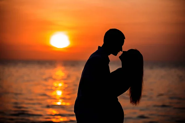 在红橙相间的夕阳西下 情侣们在靠近大海的地方亲吻 — 图库照片