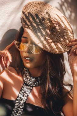 Beyaz sütyenli ve mavi şortlu Afrikalı bir kız güneşli bir palmiye bahçesinde büyük palmiye ağacının yanında duruyor.