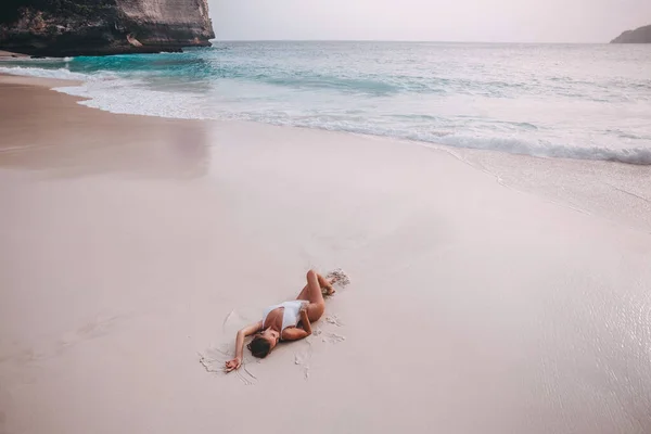 一名苗条的小女孩躺在努沙佩尼达岛海边一个空旷的开林金海滩上的柔和的粉红沙滩上 — 图库照片