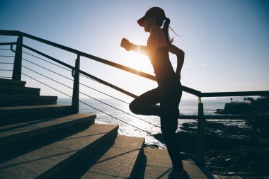 Spor salonundaki kadın koşucu deniz kenarındaki merdivenlerde koşuyor.
