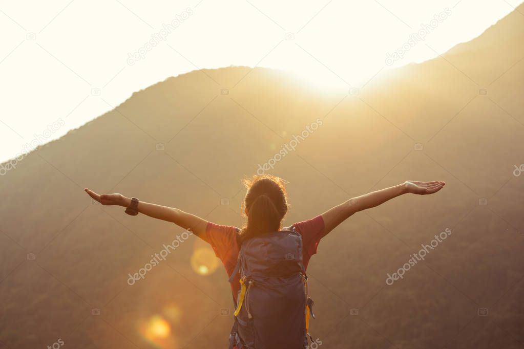 successful female hiker with outstreched arms standing on mountain top during sunrise