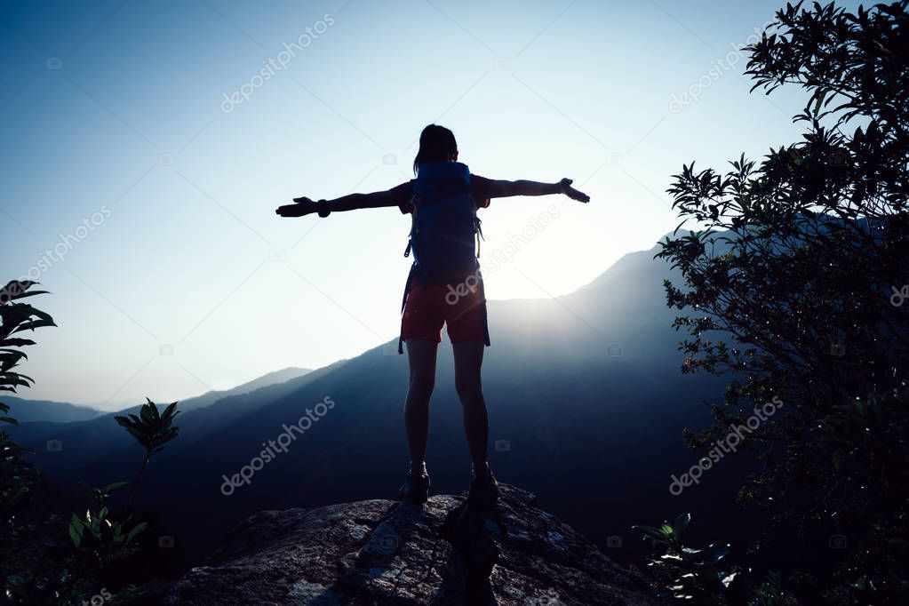 successful female hiker with outstreched arms standing on mountain top during sunrise