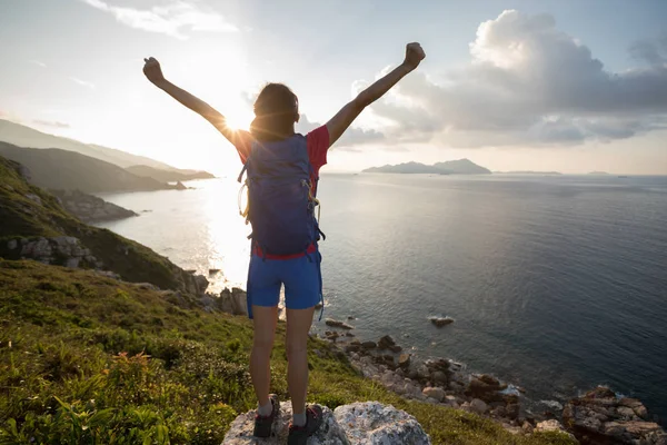 Cheering woman enjoying nature with opened arms on seaside cliff