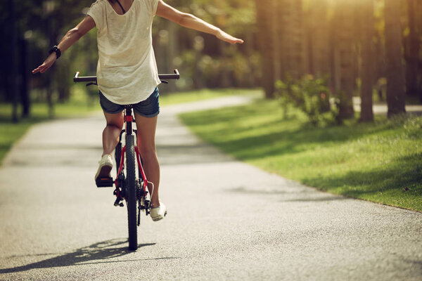 Женщина на велосипеде по тропе в солнечном парке с распростертыми руками
