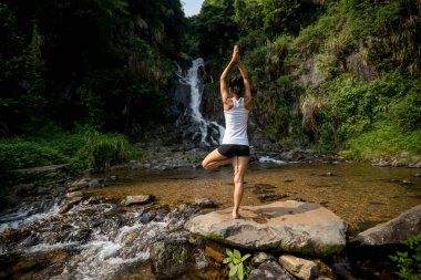Genç kadın şelale orman içinde yakınındaki yoga yaparken