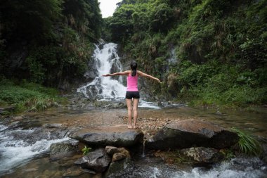 Şelale orman içinde karşı ayakta kollarını açarak genç kadın