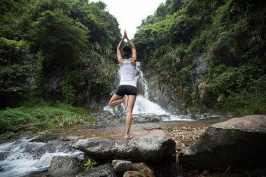 Genç kadın şelale orman içinde yakınındaki Yoga uygulamak