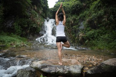 Genç kadın şelale orman içinde yakınındaki Yoga uygulamak