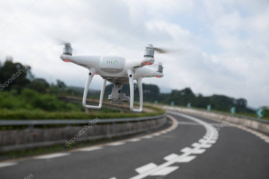 White drone with camera flying over highway
